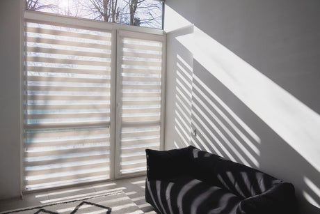 Sunlight filtering through zebra blinds, casting soft shadows on a sofa and floor, highlighting their stylish design and light control.