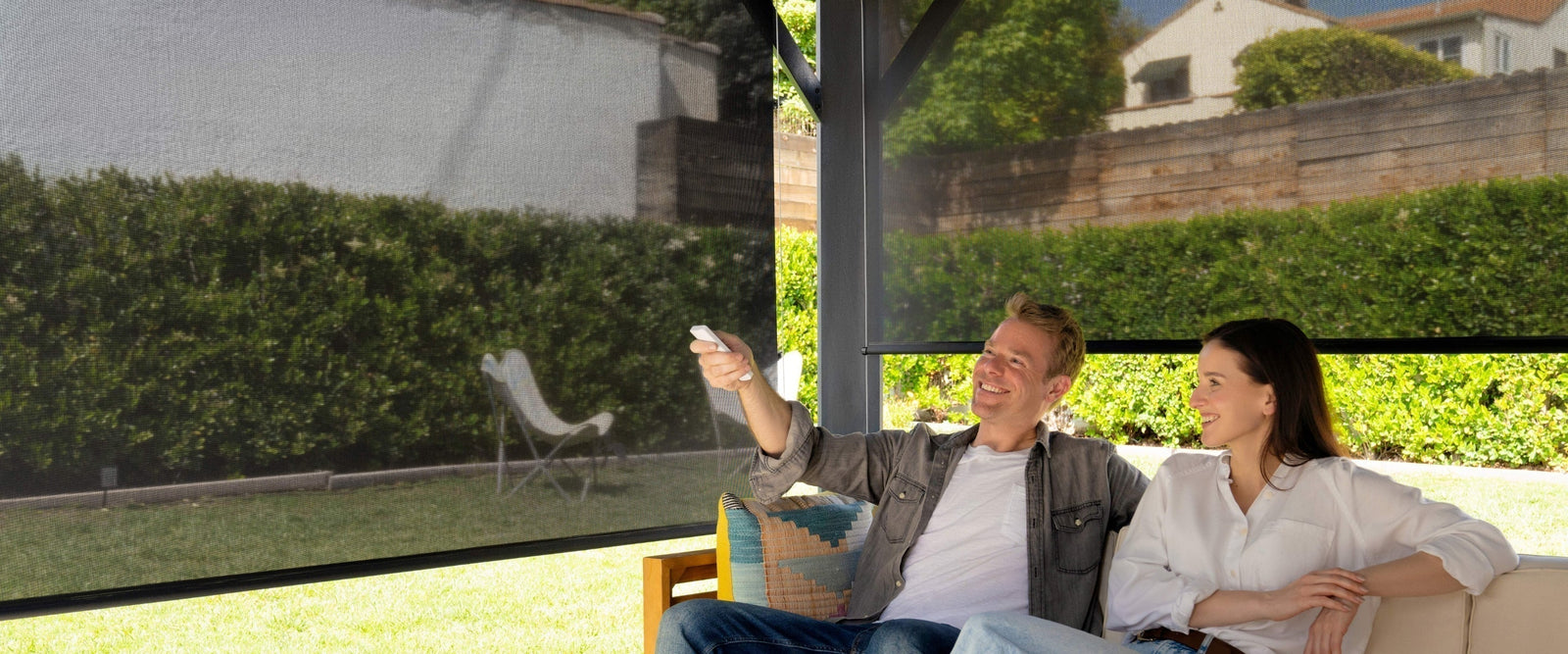 Couple relaxing in their backyard while using a remote to adjust outdoor shades, enhancing comfort and sun protection.
