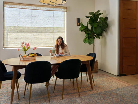 woman reading a book and drinking coffee at dining table with motorized woven wood shades behind